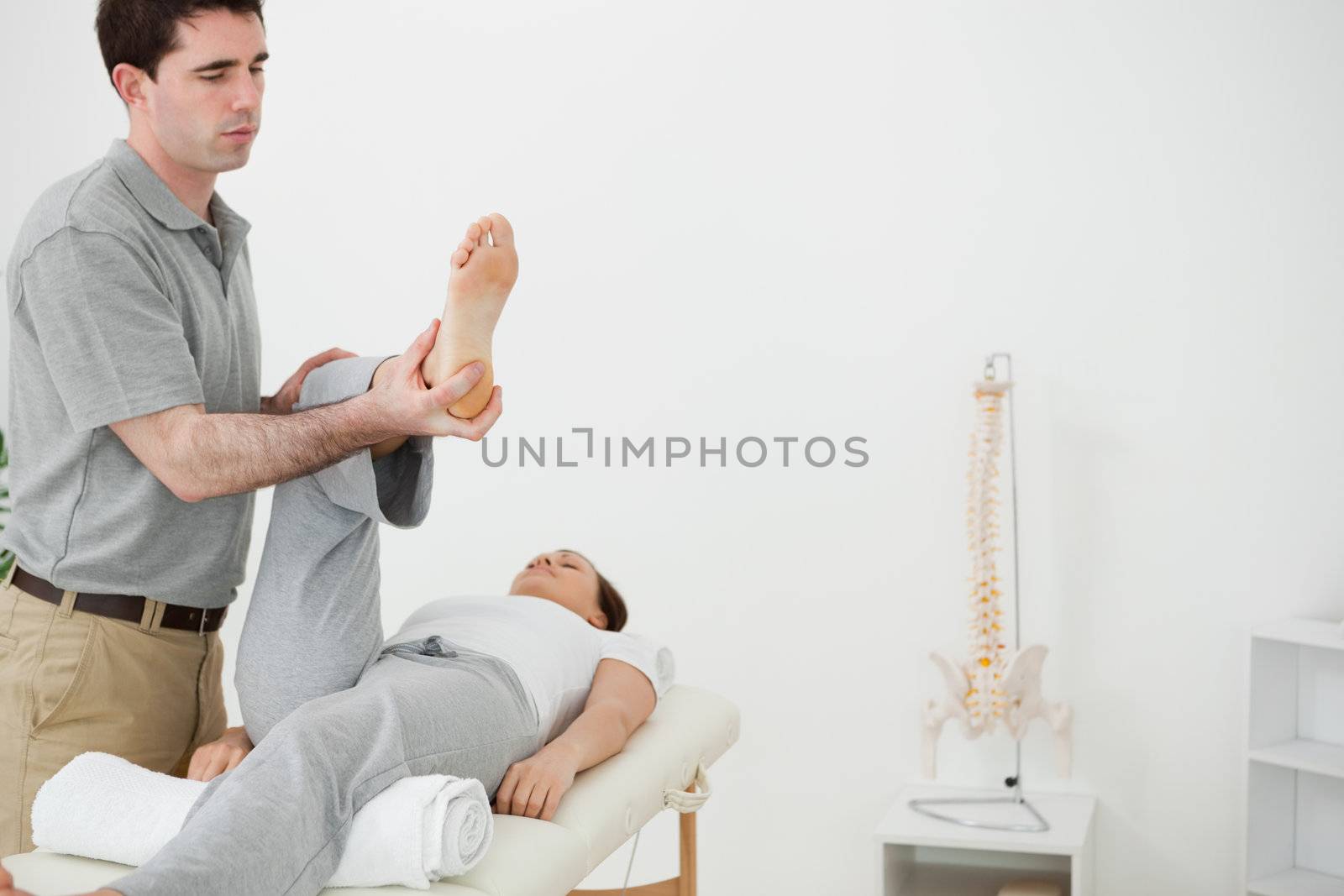 Brunette physiotherapist manipulating the leg of a woman in a room