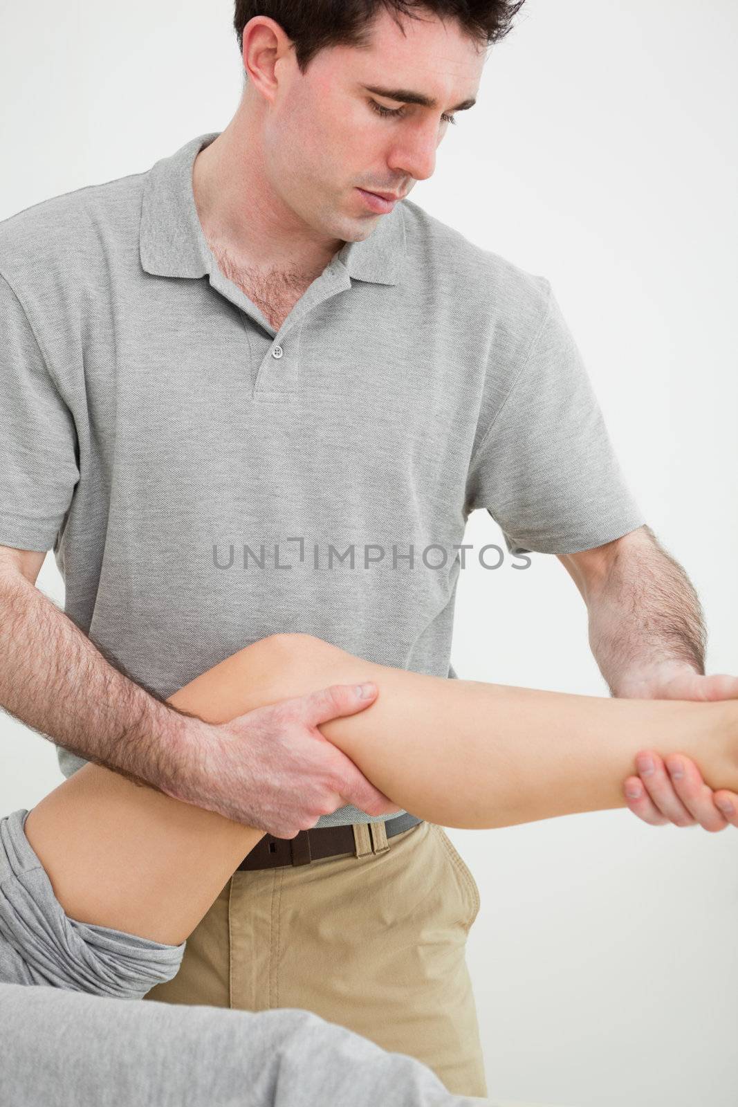 Serious osteopath examining a the leg of his patient by Wavebreakmedia