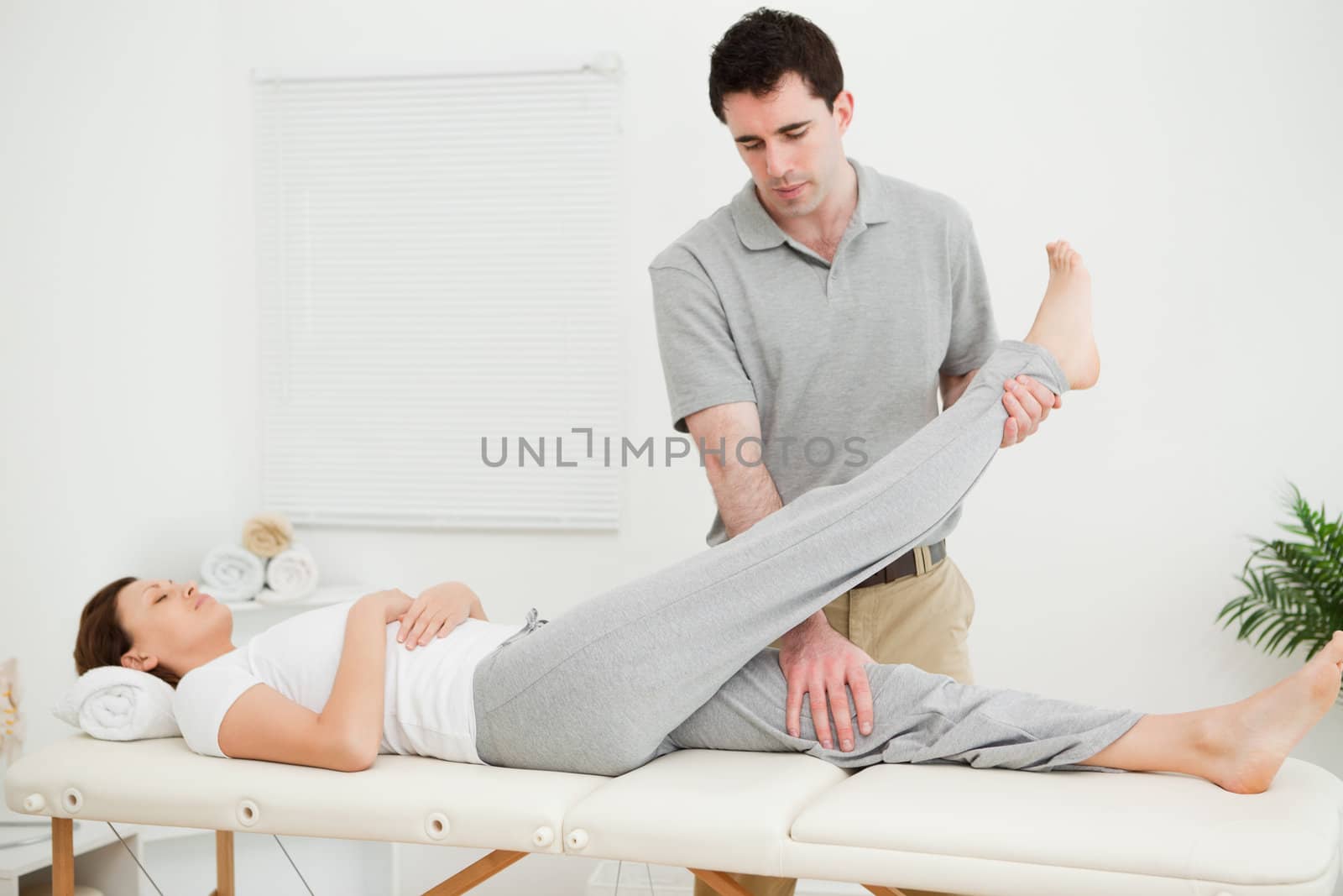 Brunette physiotherapist raising the leg of a patient in a room