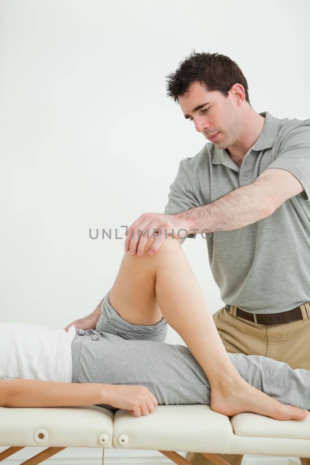 Serious physiotherapist stretching a leg while standing in a room