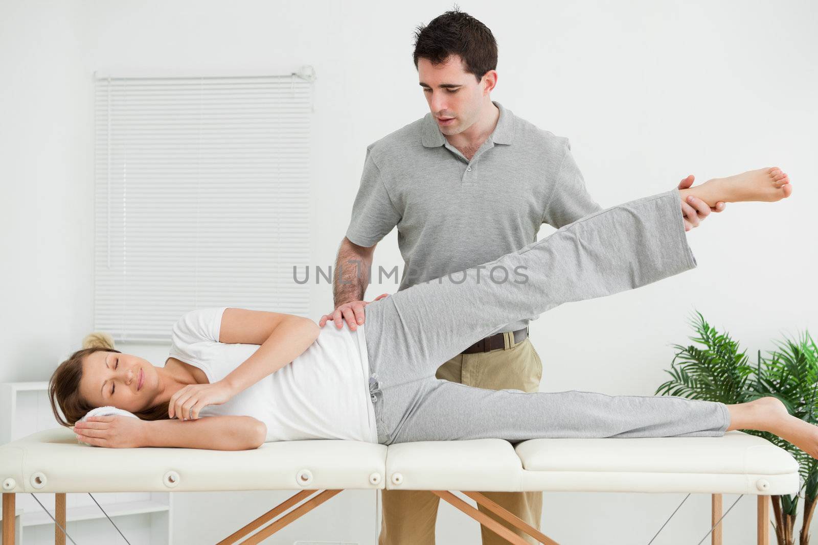 Serious practitioner rising the leg of his patient in his room