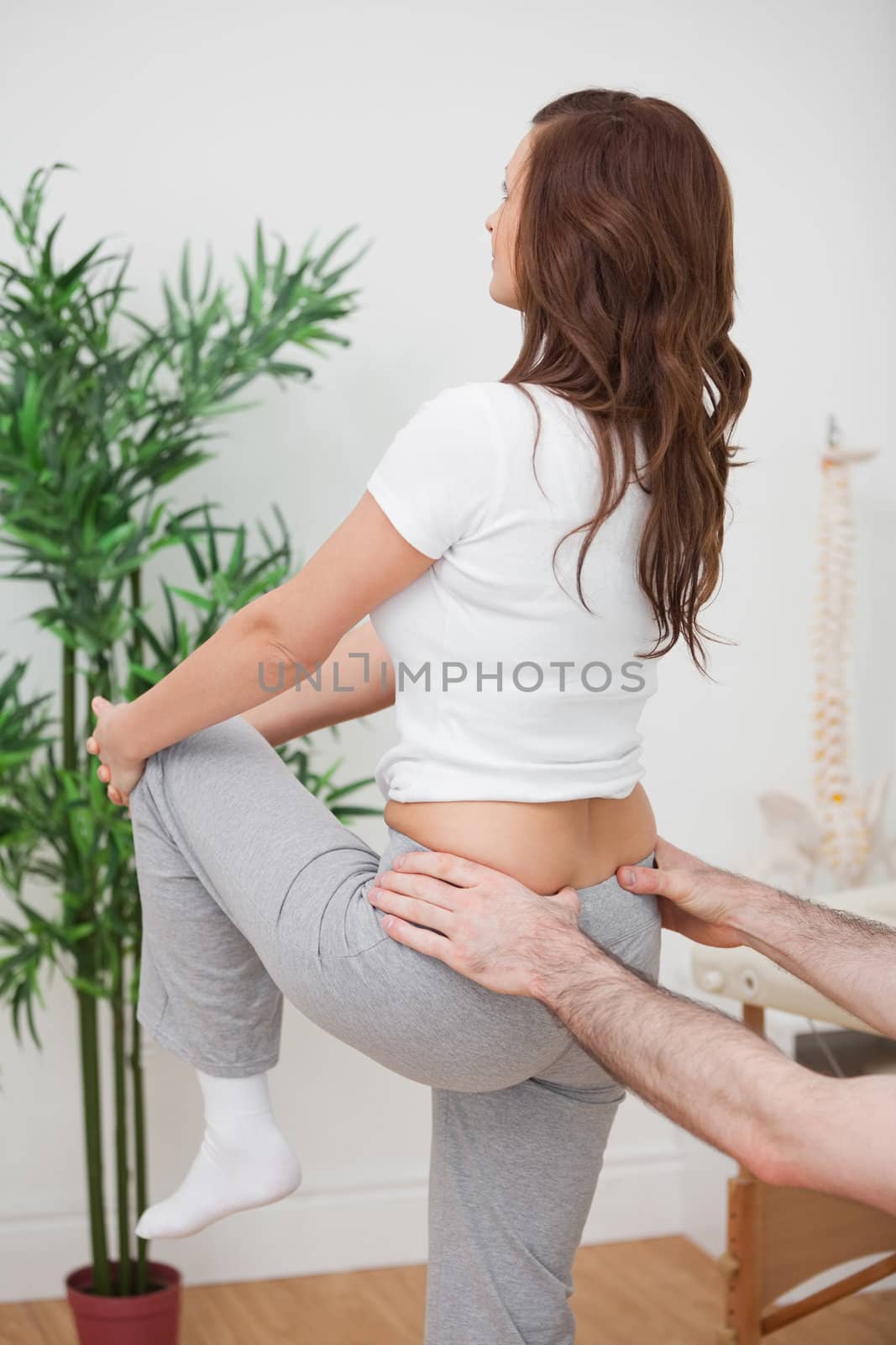 Woman stretching her leg while a man is touching her back in a room