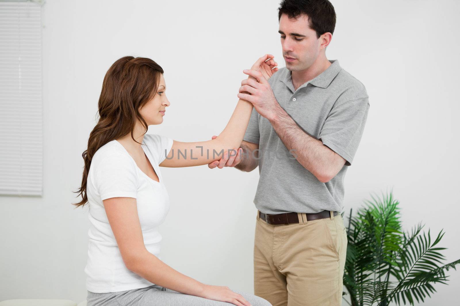 Serious physiotherapist looking at the arm of a woman in a medical room