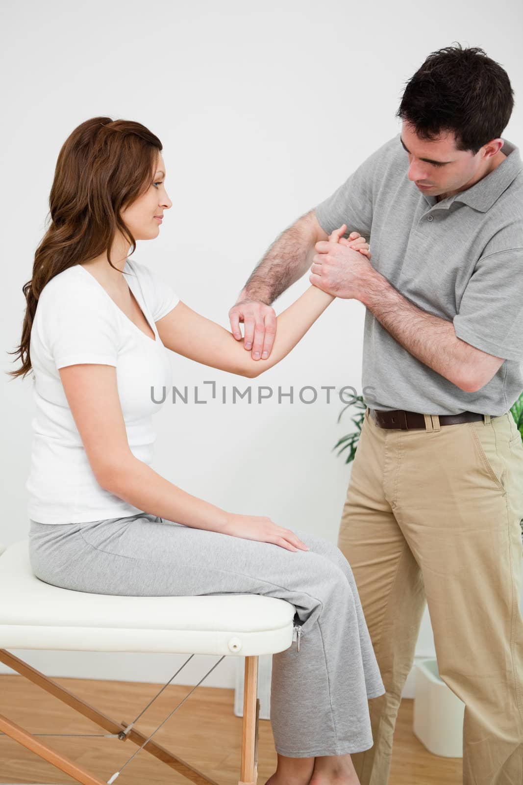 Serious physiotherapist touching the elbow of a woman in a room