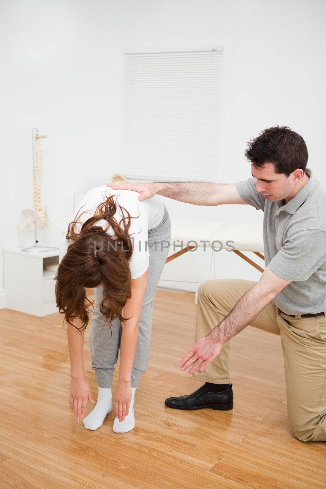 Doctor looking at a patient who is doing stretching exercises in a room