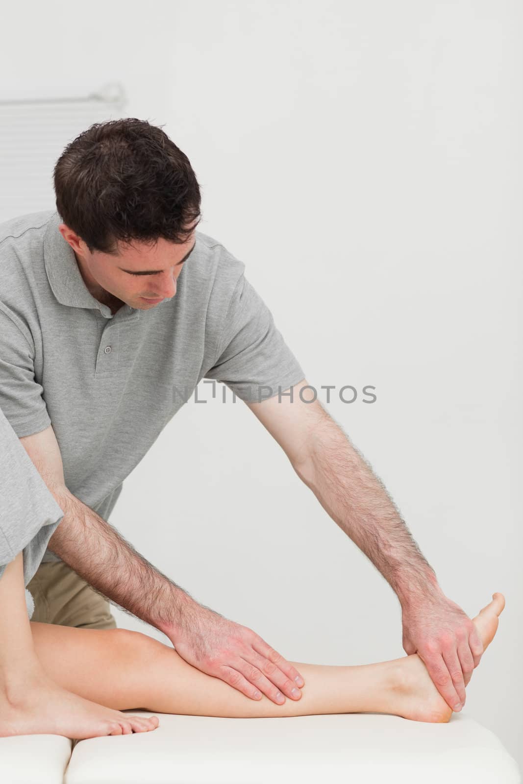Serious physiotherapist working on the calf of a patient in a room