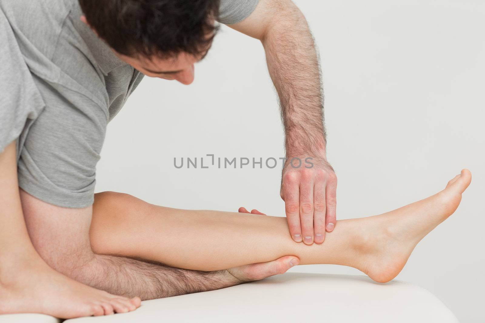 Serious osteopath massaging the shin bone of a patient by Wavebreakmedia