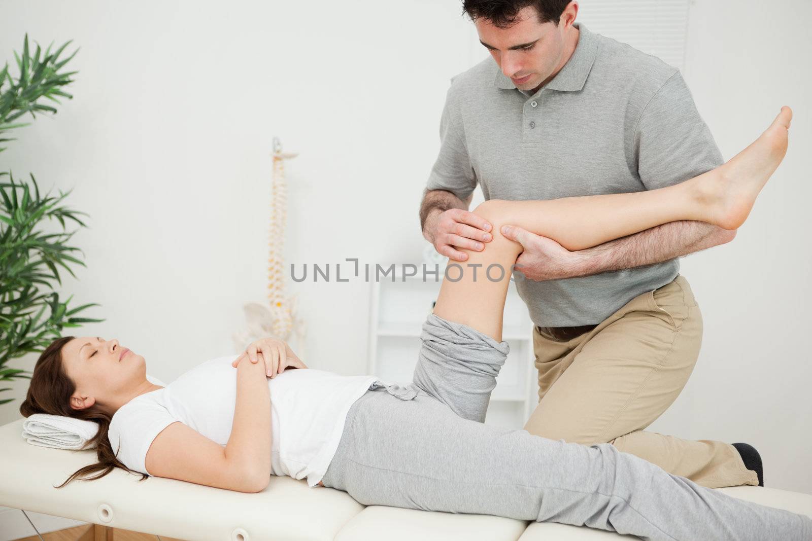 Serious osteopath bending the leg of a patient in a room