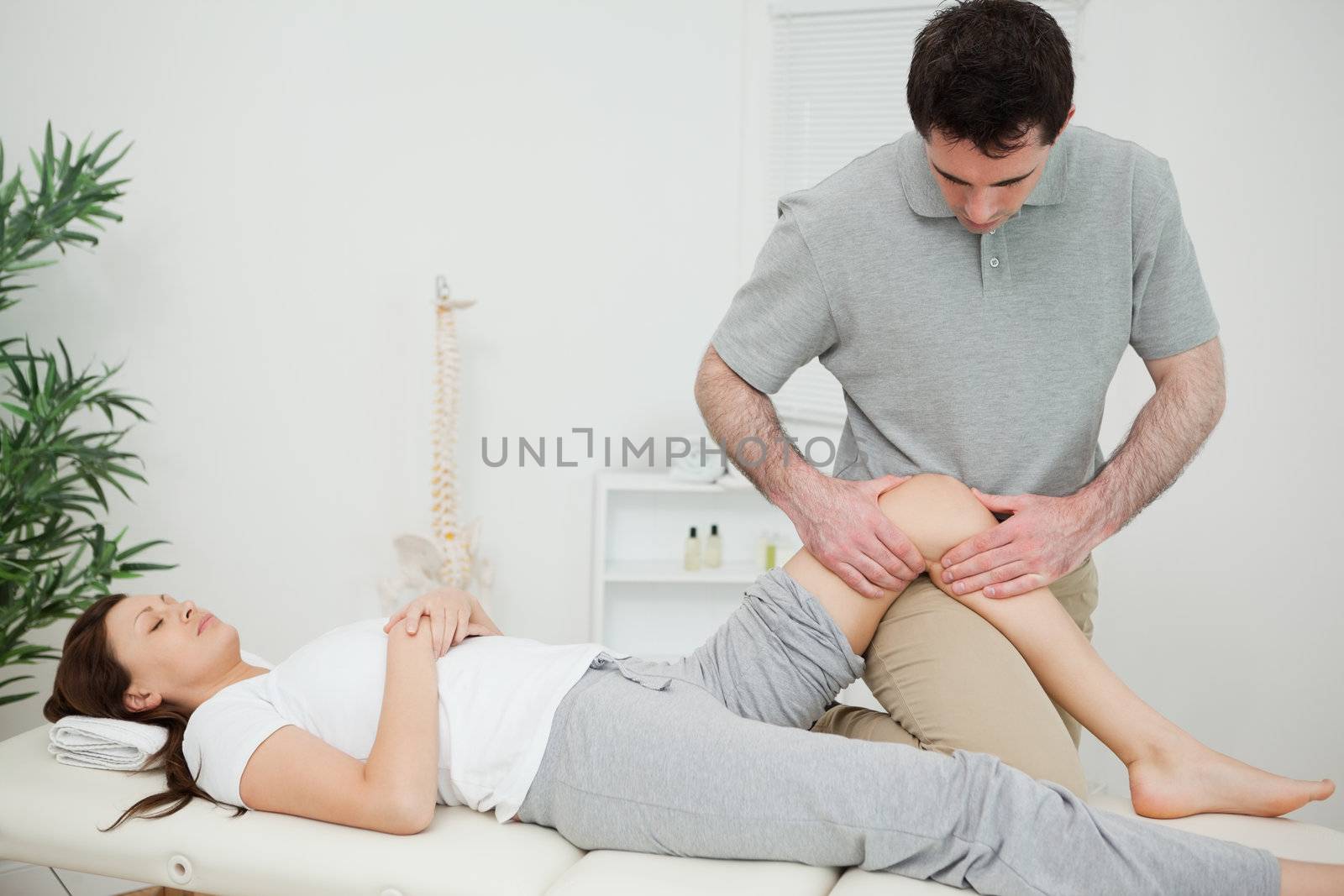 Black-haired osteopath touching the knee of a patient in a room