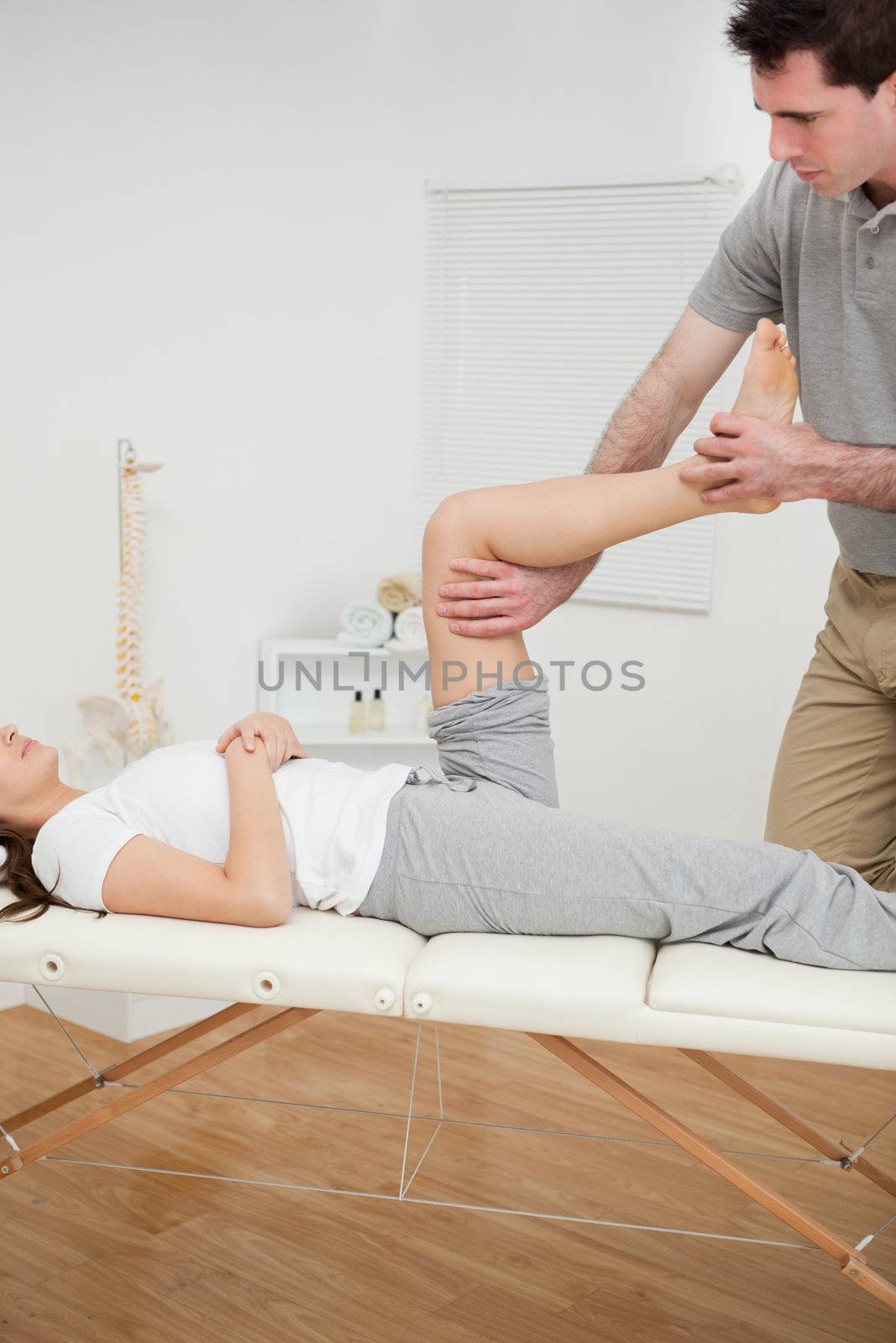 Serious osteopath bending the leg of a woman in a room