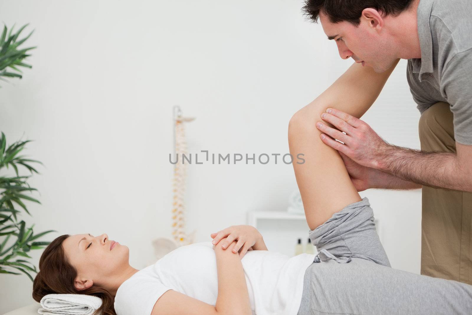 Serious physiotherapist raising a leg in a room