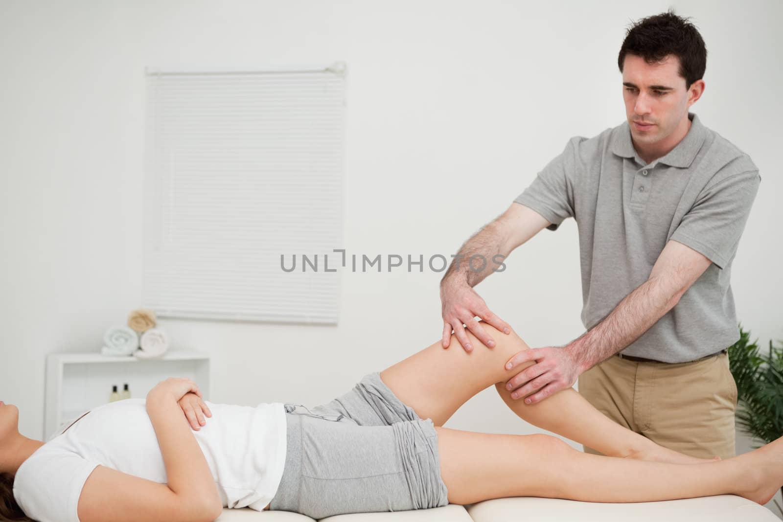 Serious doctor holding the knee of a woman in a room