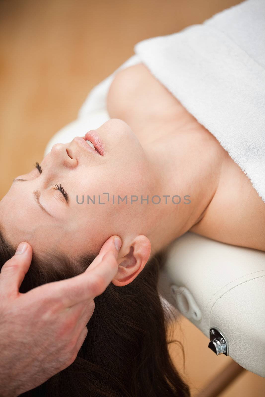 Woman lying on the back while being massaged on her head in a room