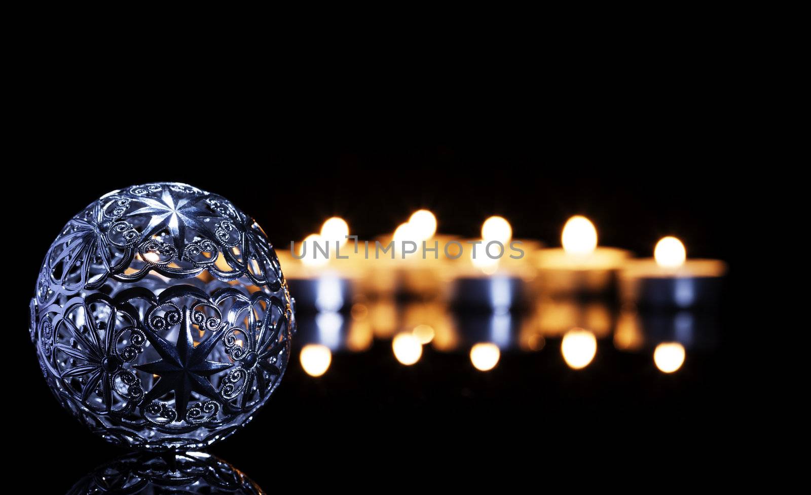 metal christmas ball in front of tea candles on a black mirror
