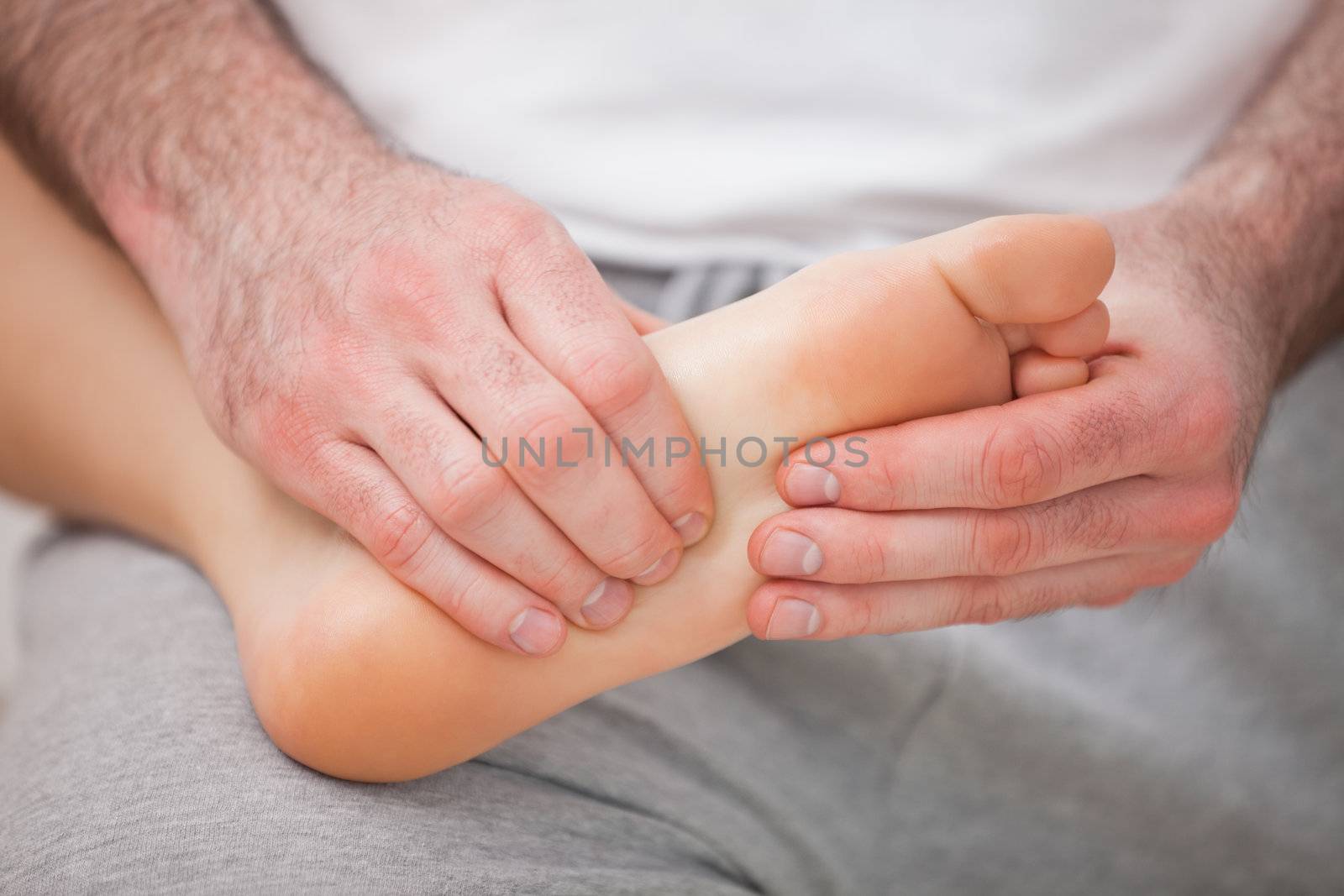 Podiatrist massaging the foot of a woman while holding it on his thigh indoors