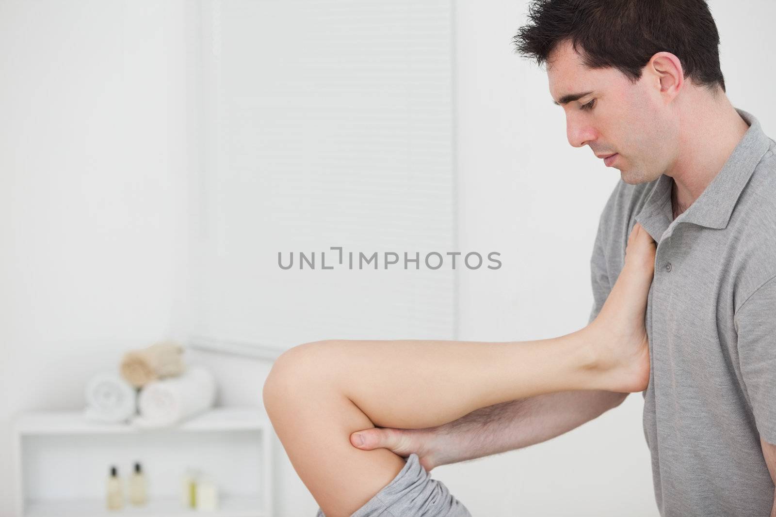 Chiropractor raising the leg of his patient against his chest by Wavebreakmedia