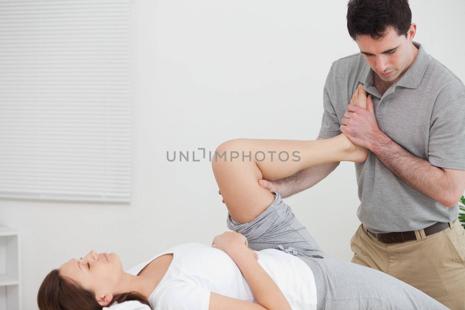 Doctor stretching the leg of woman while raising her leg against his chest indoors