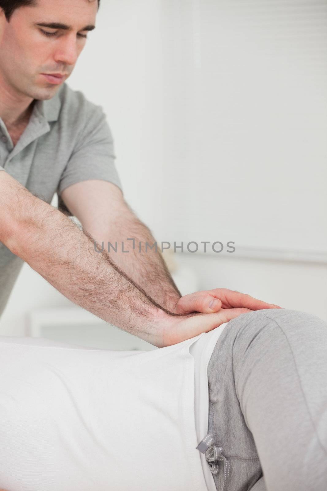 Serious chiropractor pressing the hip of his patient in a room