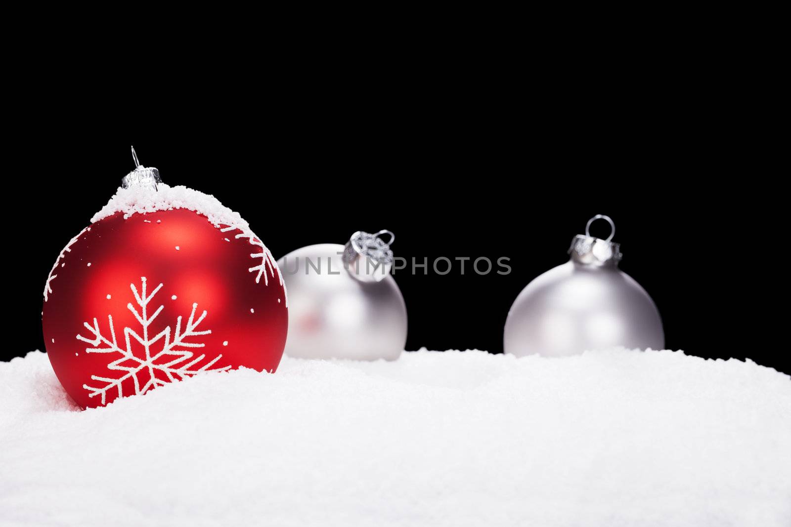 red christmas ball in front of silver christmas balls in snow with black background