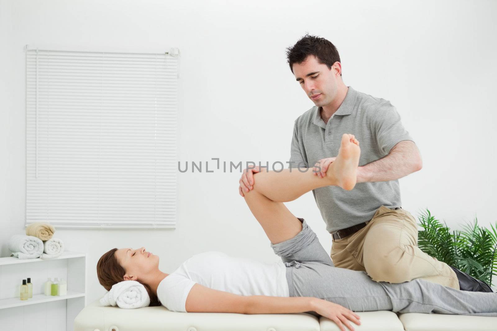 Chiropractor stretching the leg of his patient while holding it in a medical room