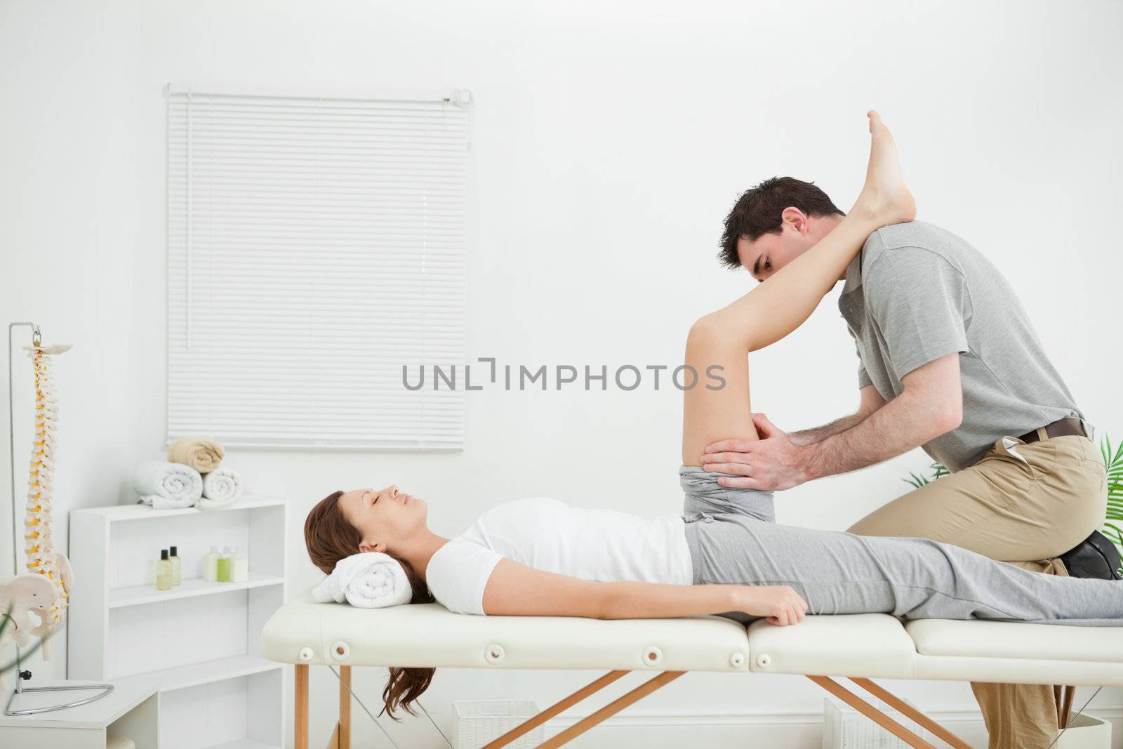 Doctor examining the thigh of a woman while putting her foot on his shoulder indoors