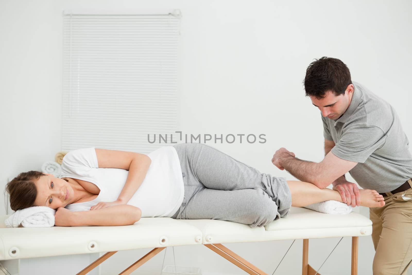 Doctor manipulating the leg of his patient while using his elbow in a room
