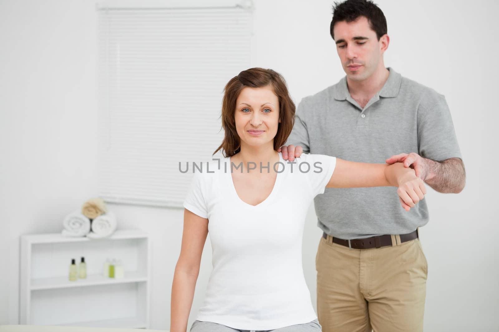 Doctor examining the shoulder of his patient while holding his arm in a room