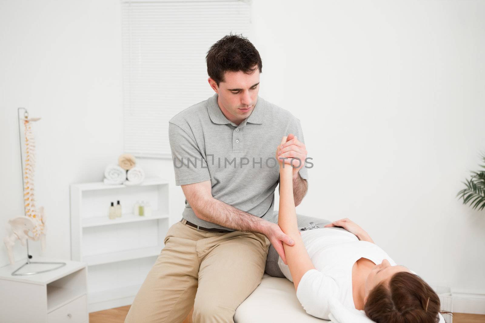 Doctor examining the arm of his patient while touching his elbow in a room
