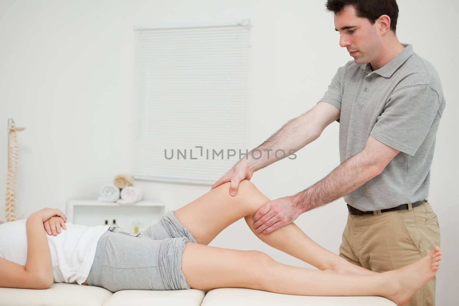 Physiotherapist examining the knee of his patient while touching it in a room