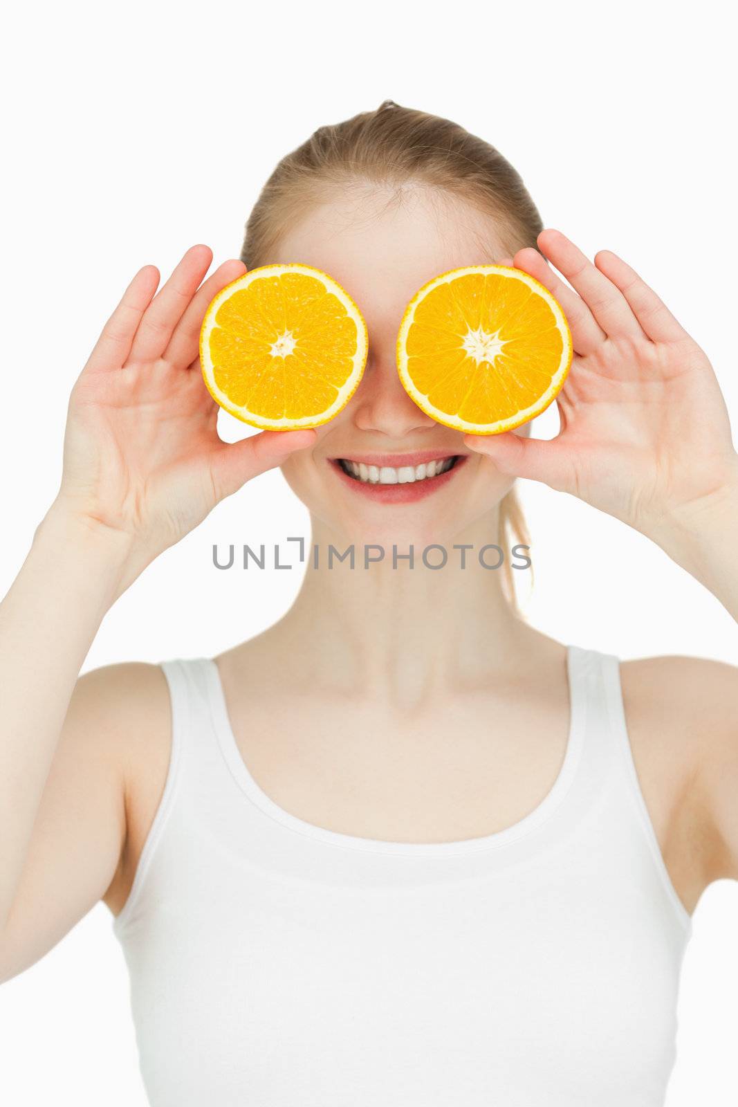 Cheerful woman placing oranges on her eyes against white background