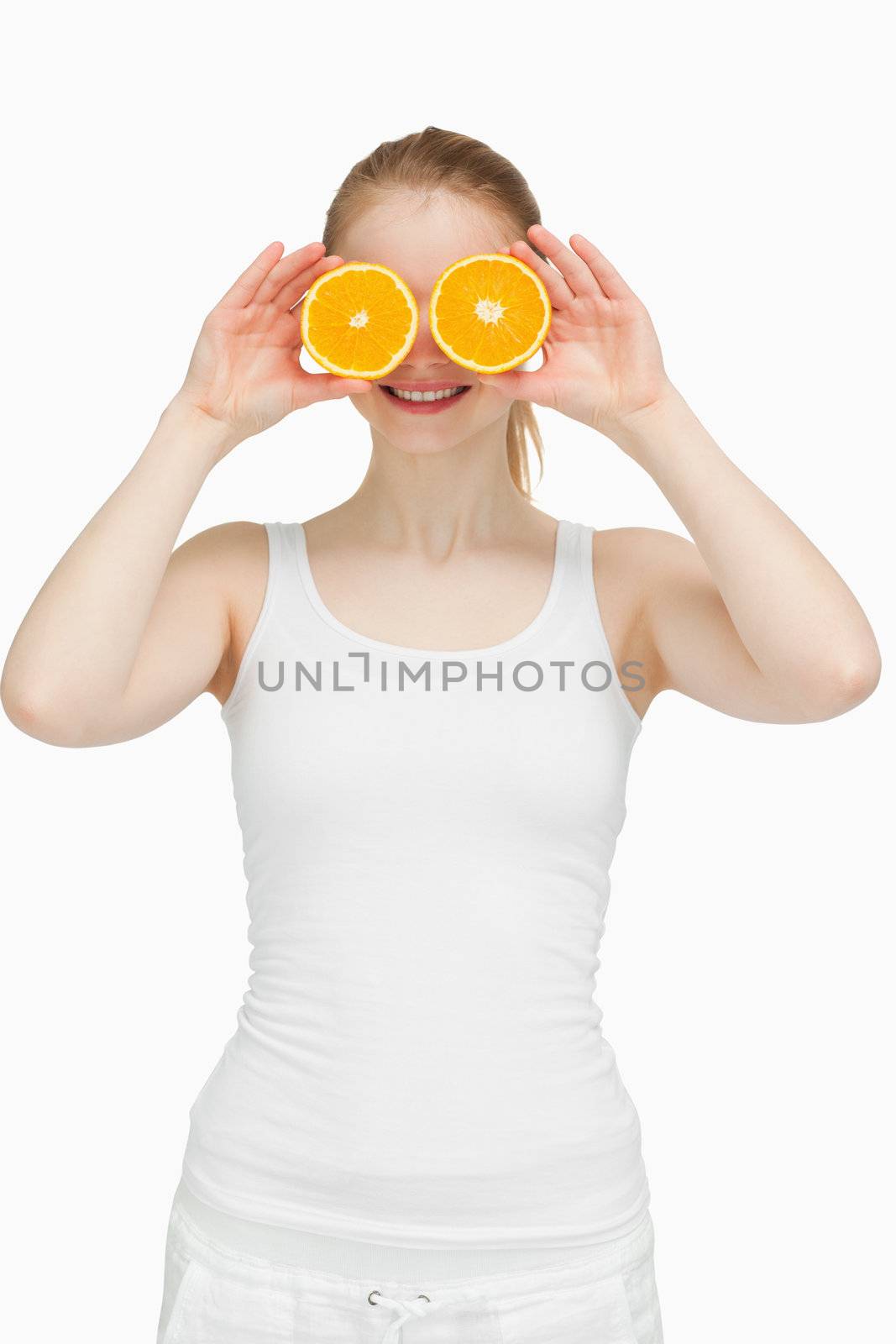 Joyful woman placing oranges on her eyes against white background