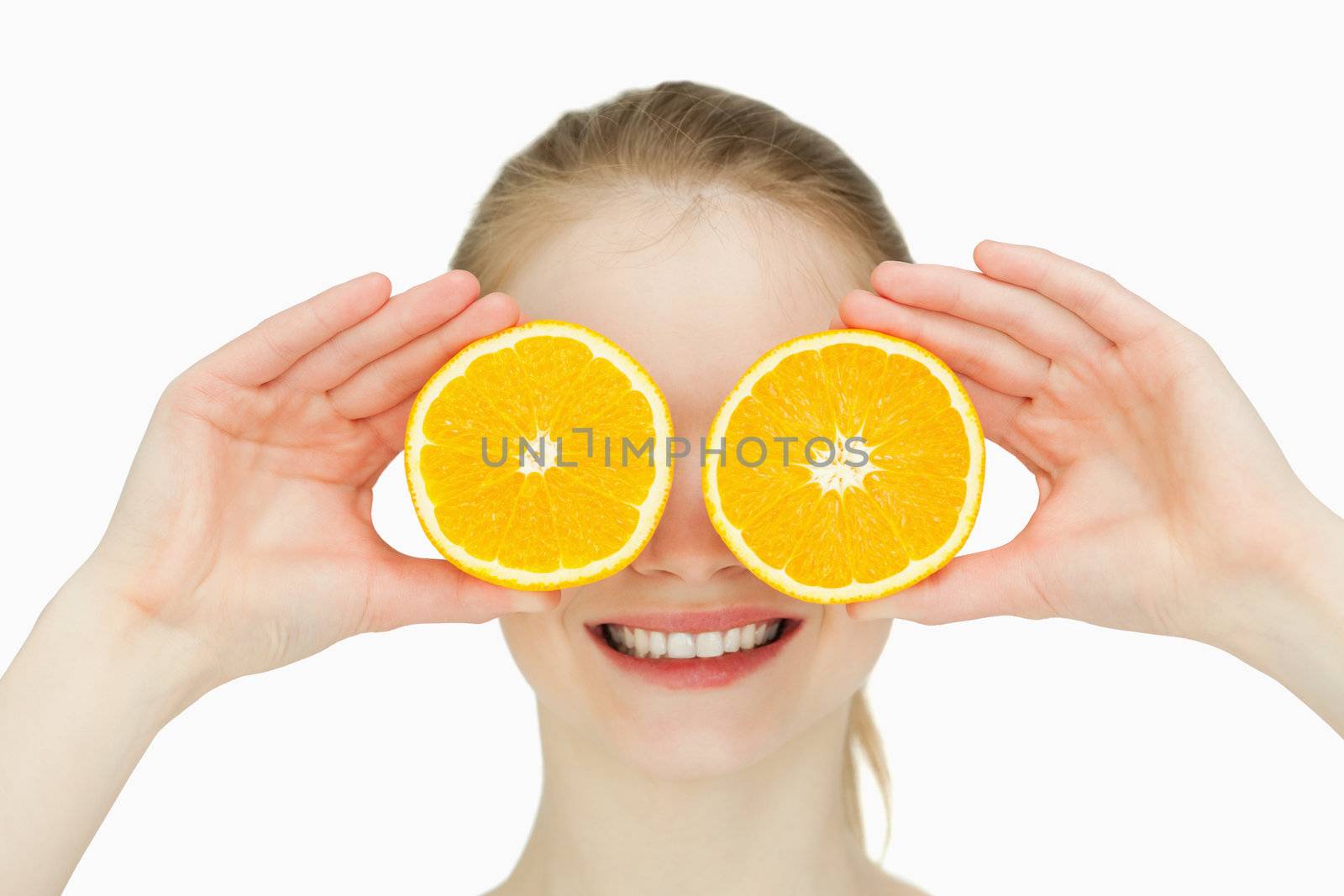 Close up of a smiling woman placing oranges on her eyes against white background