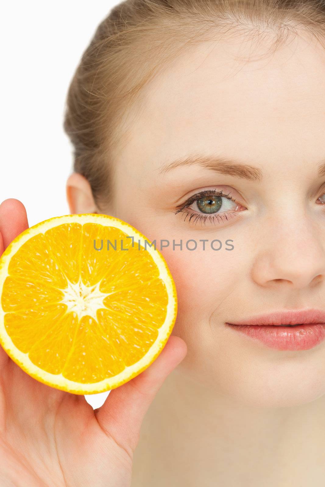 Close up of a blonde-haired girl presenting an orange against white background