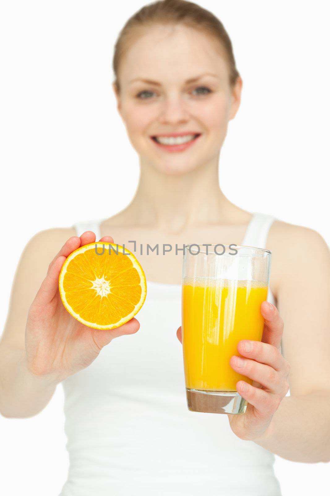 Smiling woman presenting an orange while holding a glass against white background