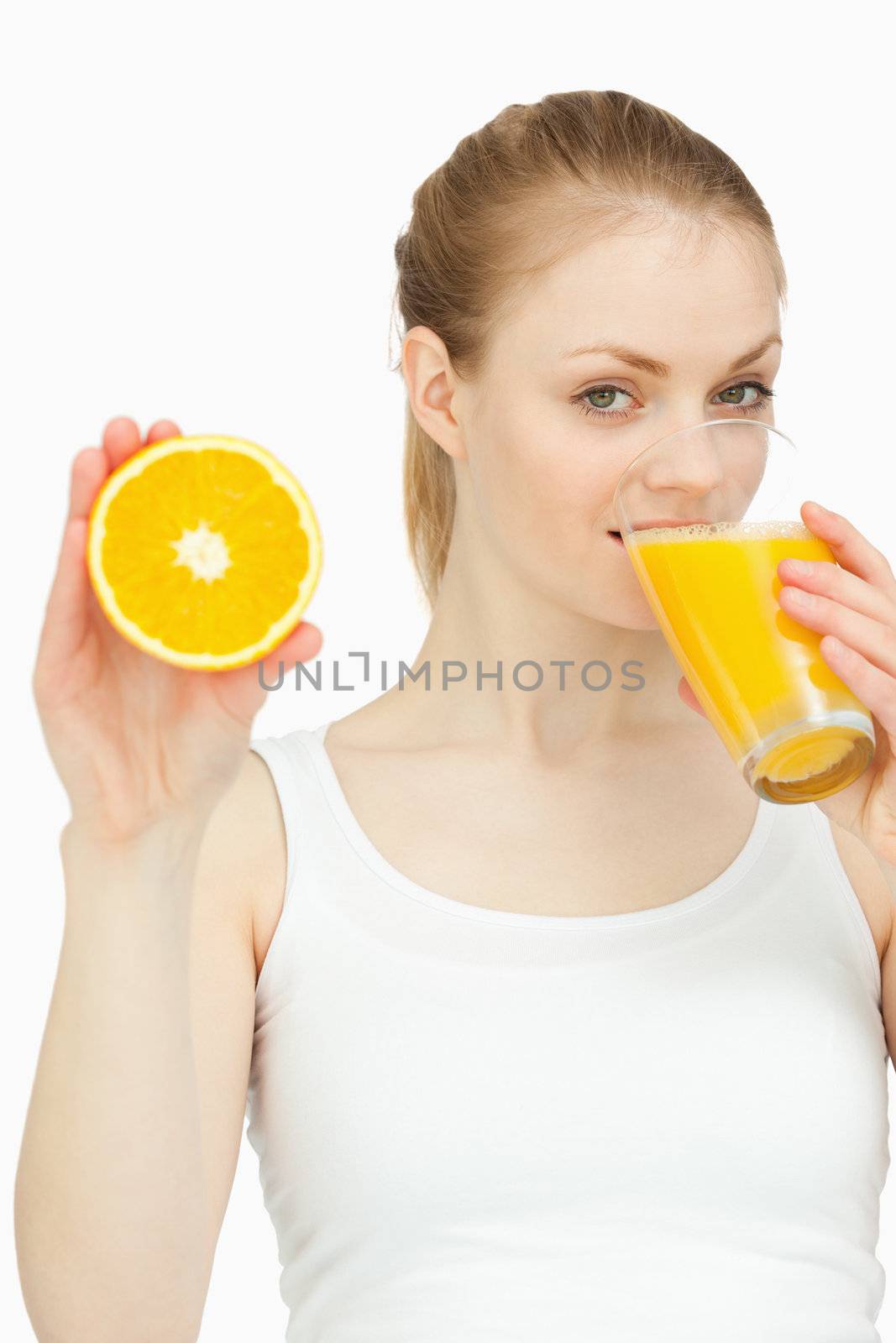 Woman drinking in a glass while presenting an orange against white background