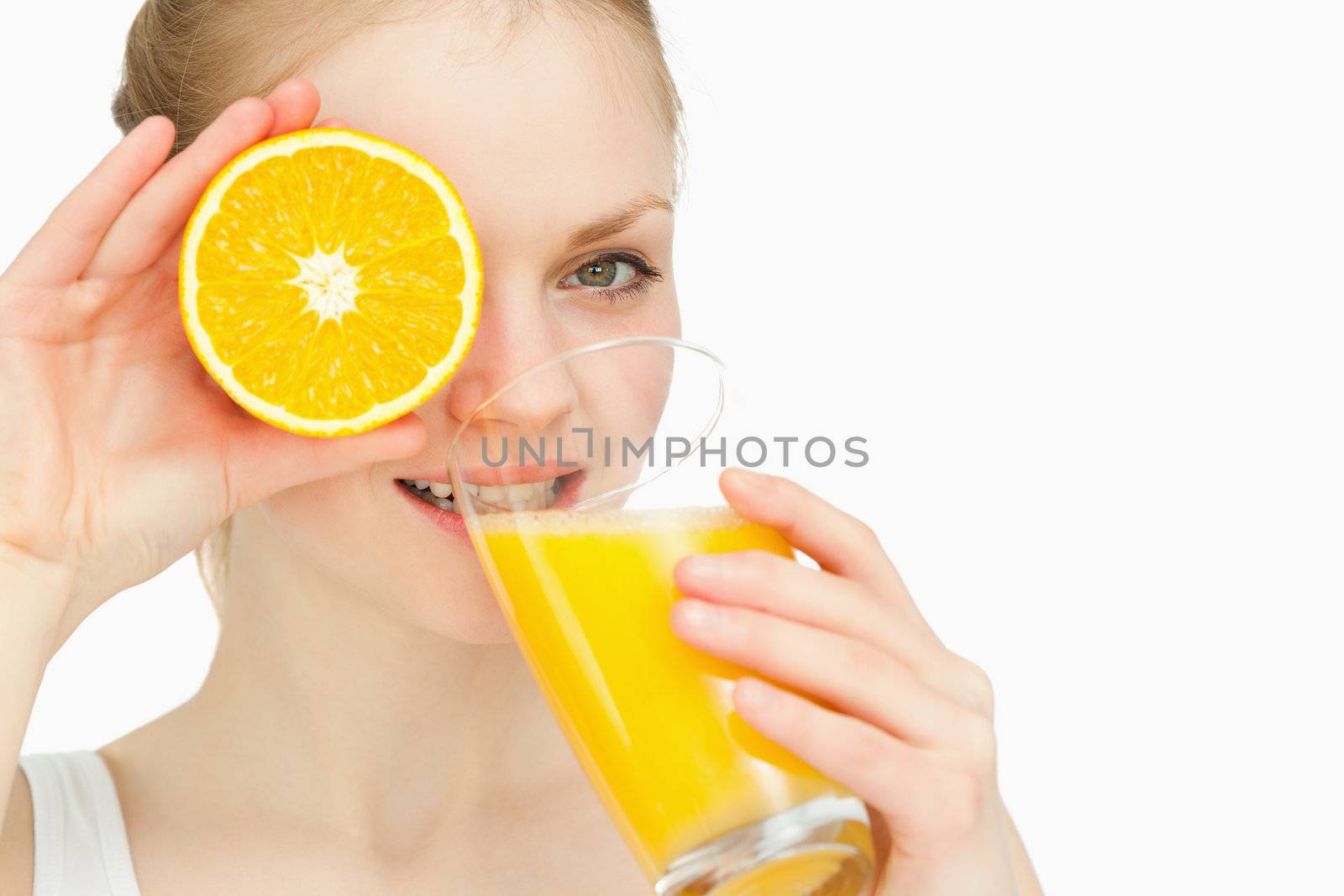 Woman placing an orange on her eye while drinking against white background