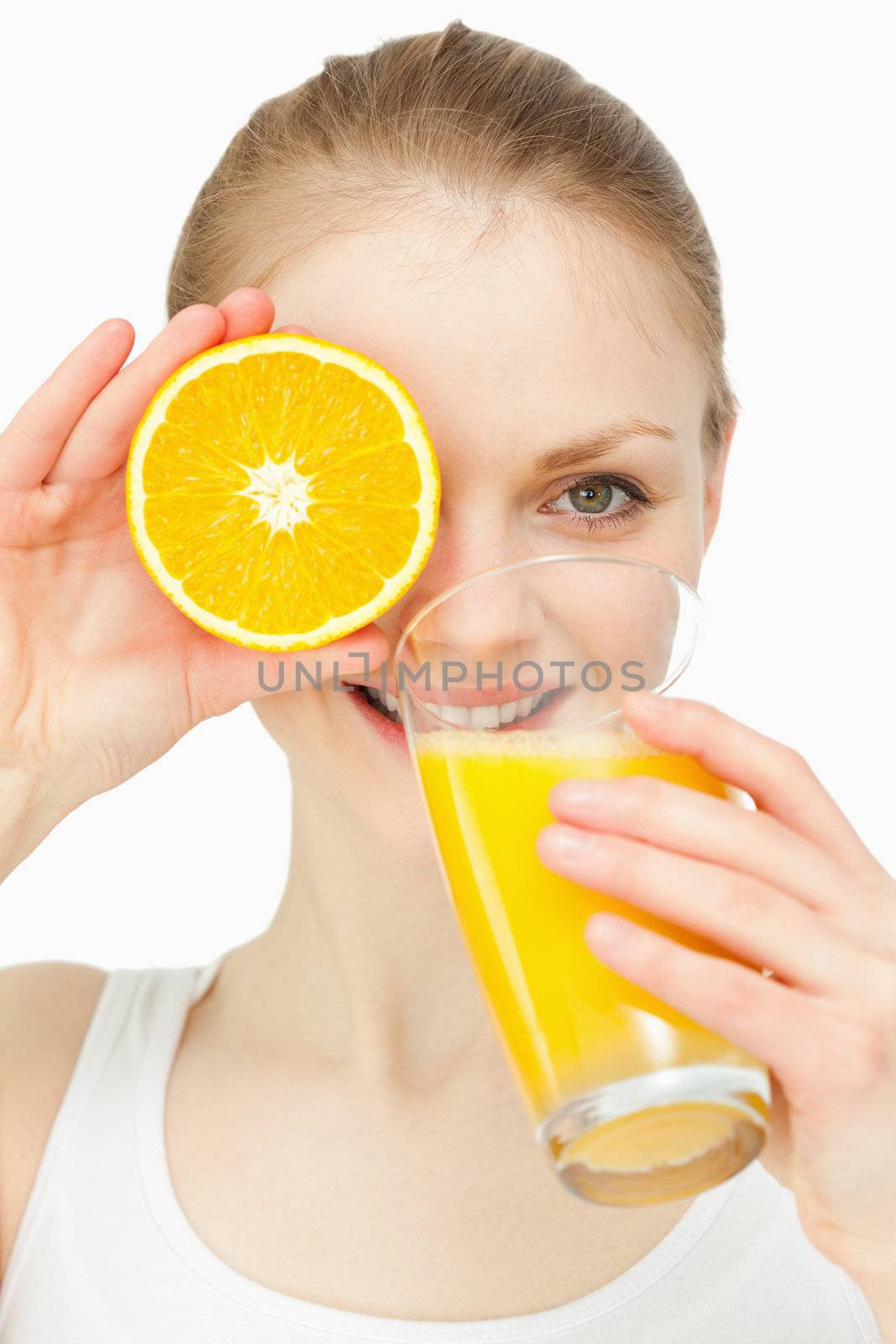 Woman placing an orange on her eye while drinking in a glass against white background