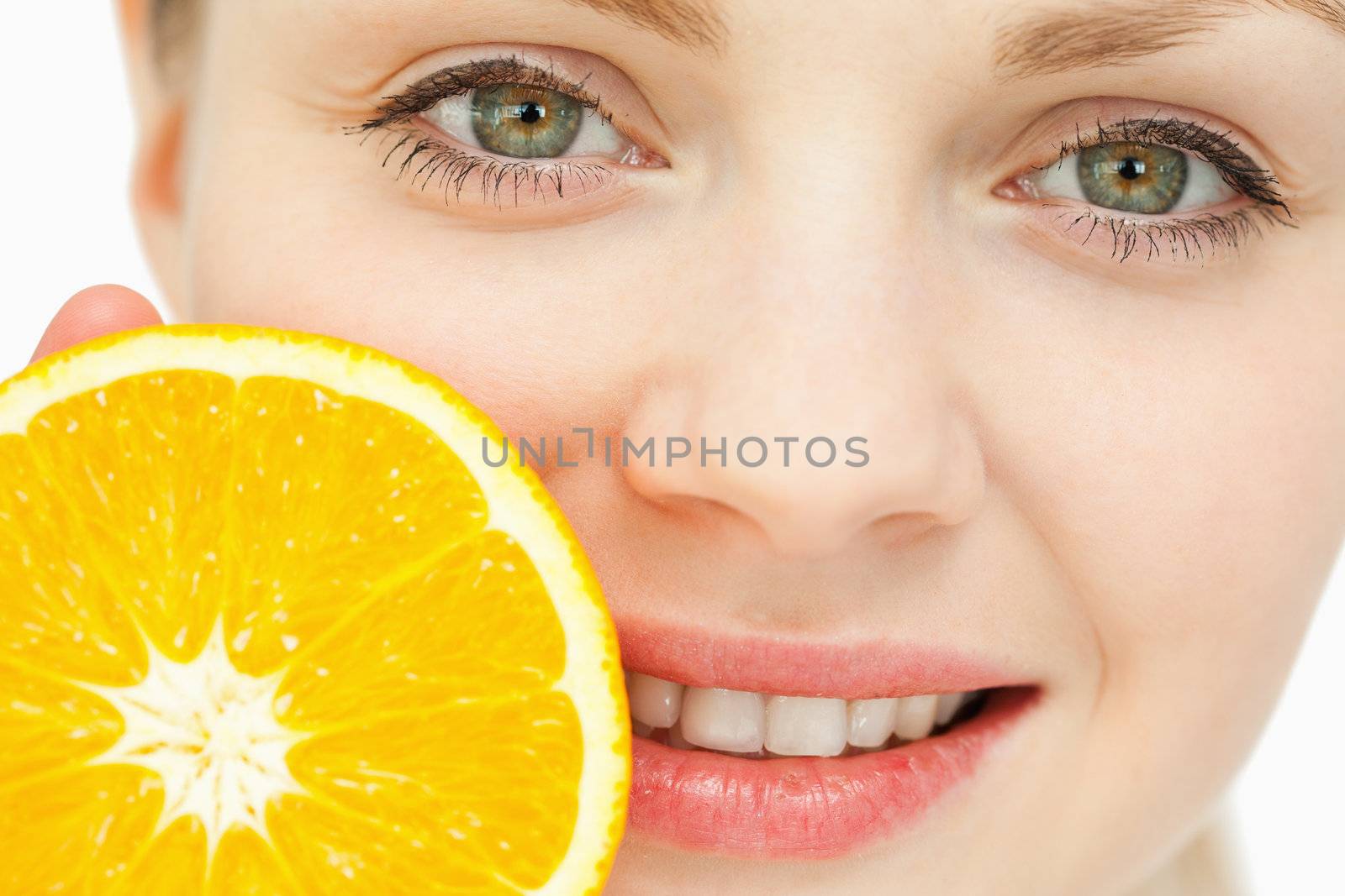 Close up of a woman placing an orange near her lips against white background