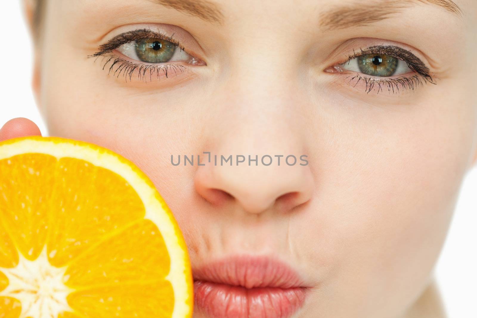 Close up of a woman placing an orange near her mouth against white background