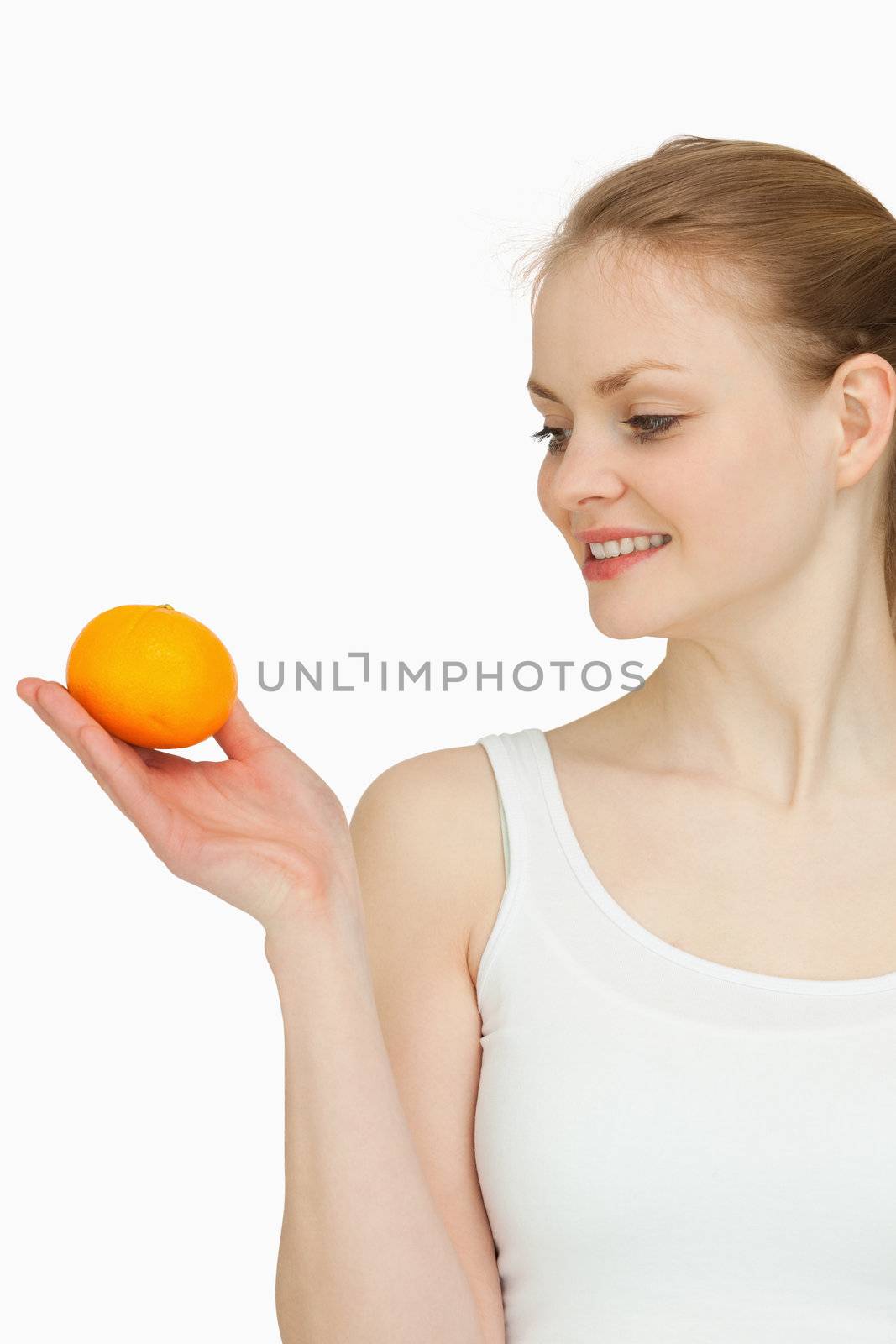 Smiling woman presenting a tangerine while looking at it against white background