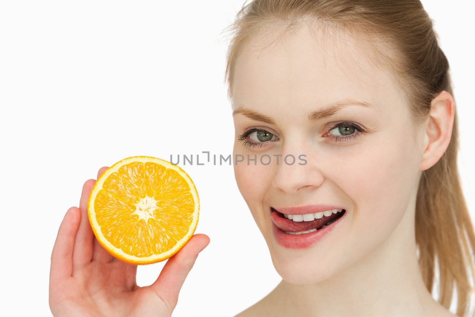 Woman holding an orange while placing her tongue on her lips against white background