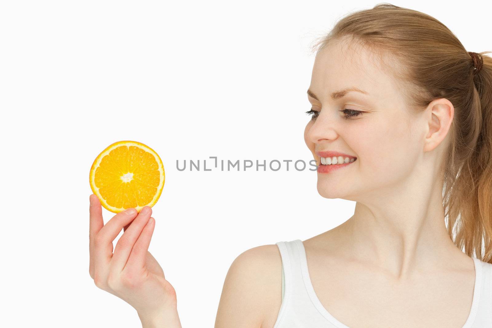 Woman presenting an orange slice while looking at it against white bakground