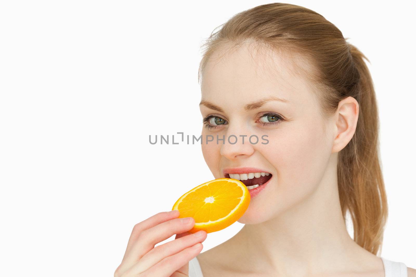 Woman placing an orange slice in her mouth against white background