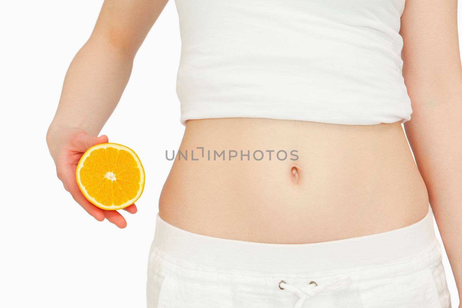 Woman placing an orange next to her belly against white background
