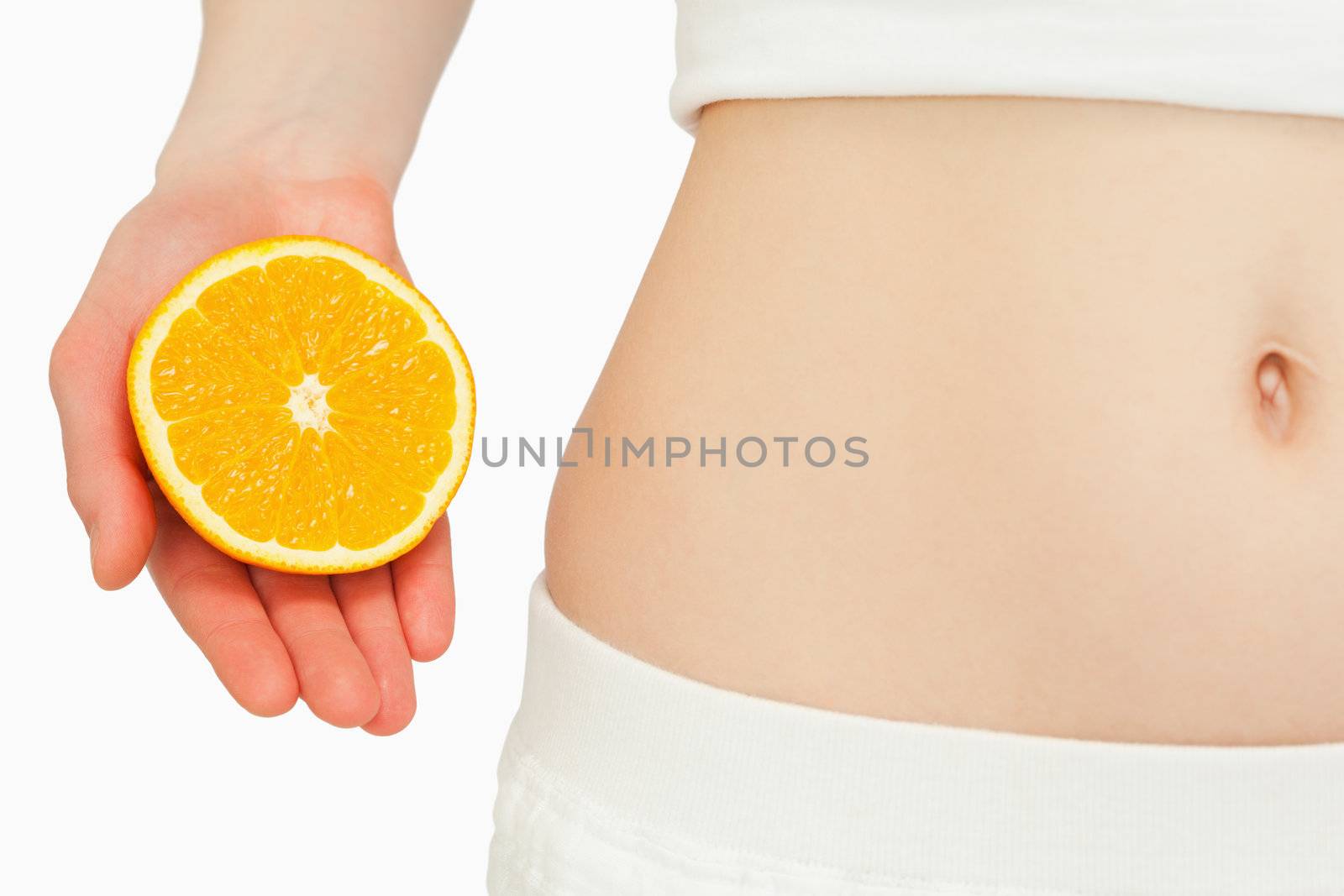 Woman placing an orange near her belly against white background