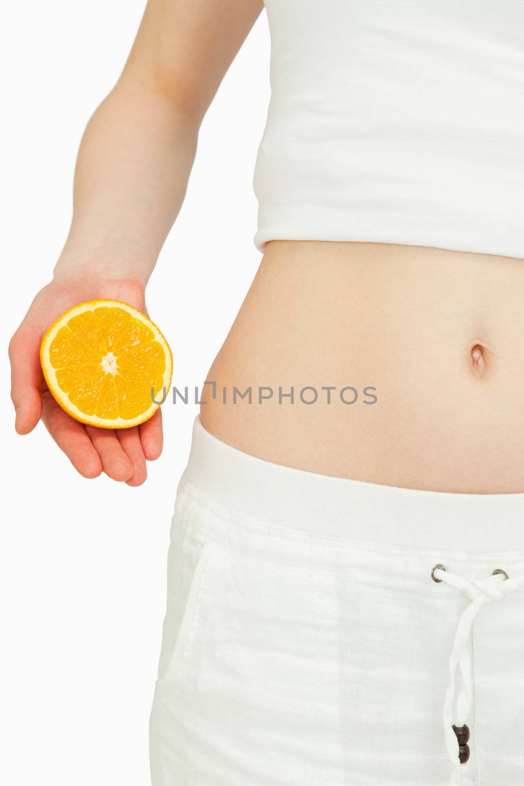 Close up of a woman placing an orange near her belly against white background