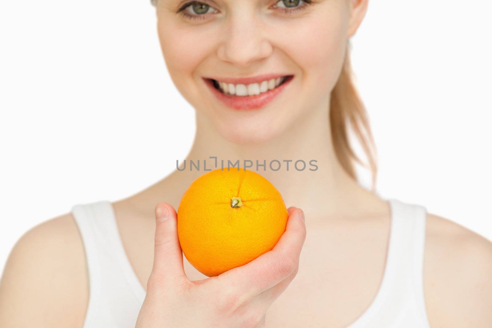 Close up of a woman holding an orange while smiling against white background