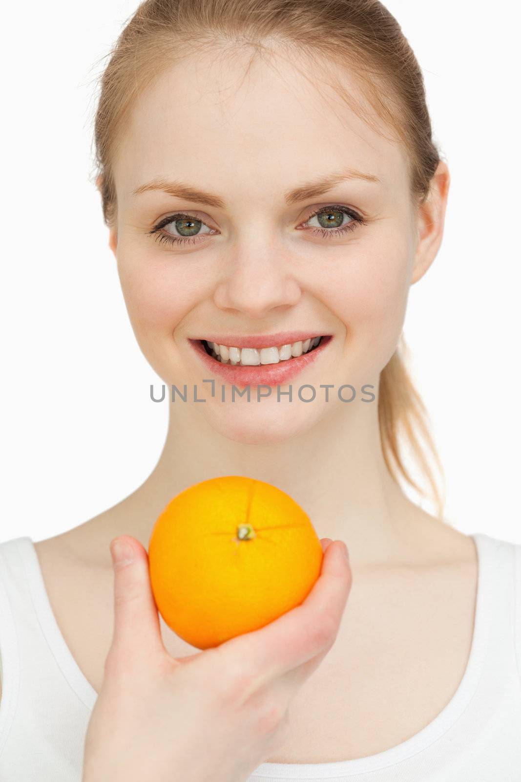 Close up of a woman presenting an orange while smiling against white background