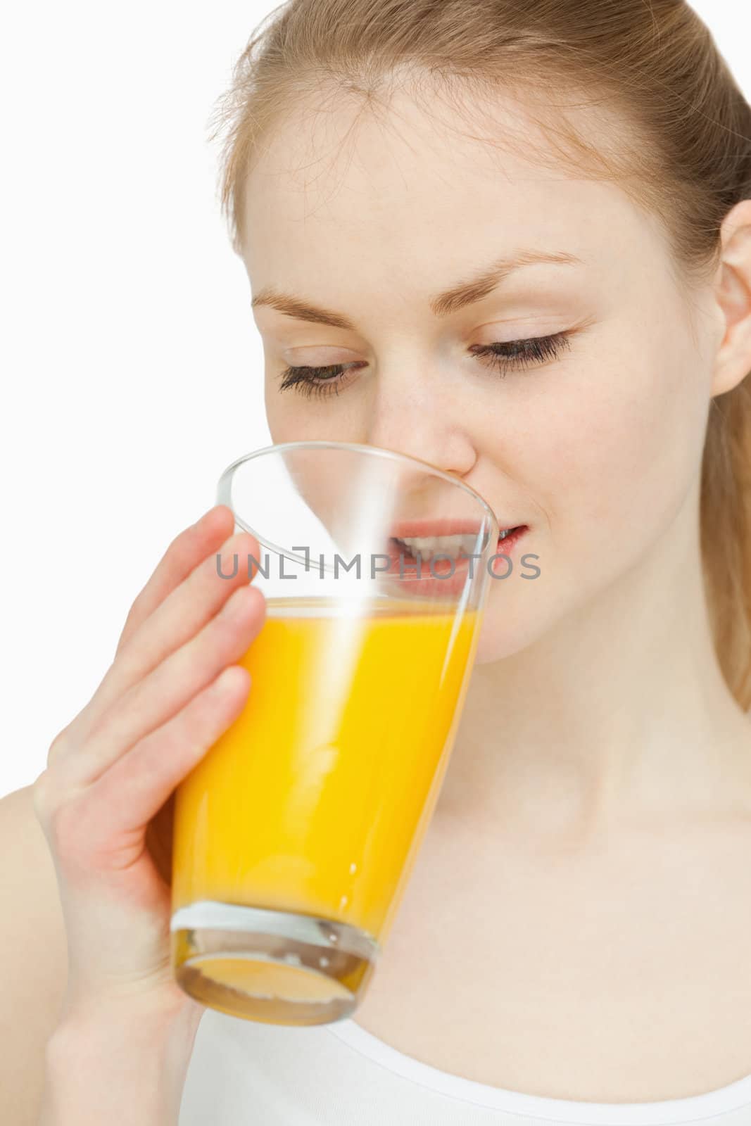 Woman drinking a glass of orange juice while looking at it against white background