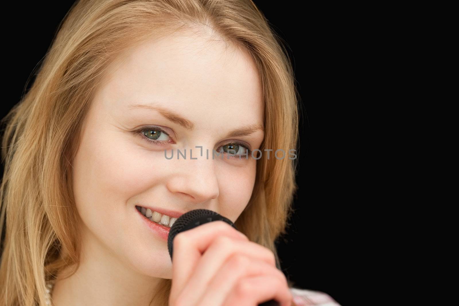 Young woman smiling while singing against black background